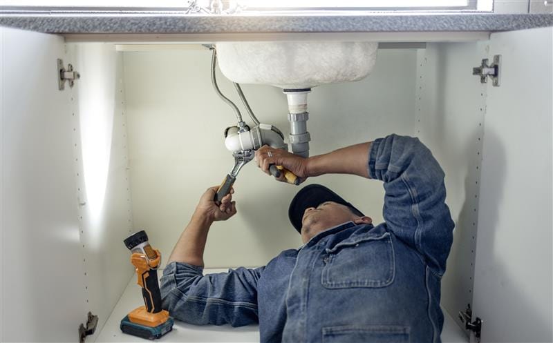 Plumber repairing pipes beneath a bathroom sink in Fort Collins