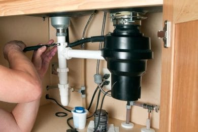 Plumber repairing a garbage disposal beneath a kitchen sink in Fort Collins