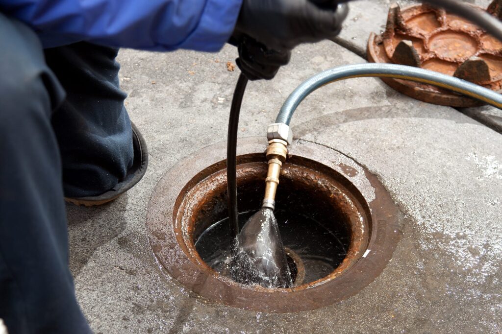 Plumber hydro jetting a sewer line through a manhole in Fort Collins