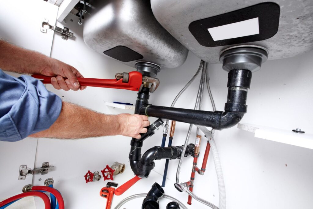 Plumber repairing drain pipes beneath a kitchen sink in Fort Collins